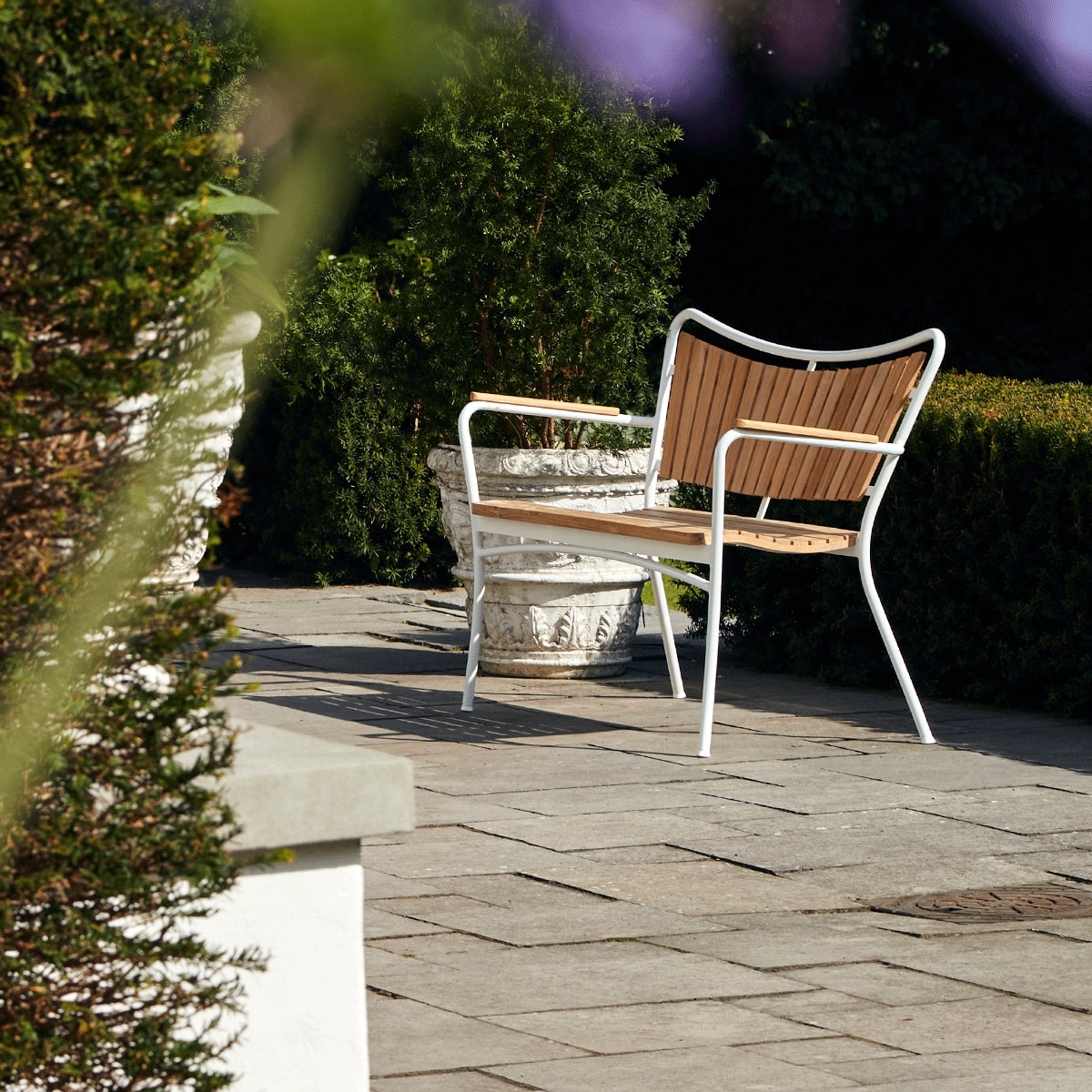 Havebænk i træ med hvidt stel, står på stenterrasse