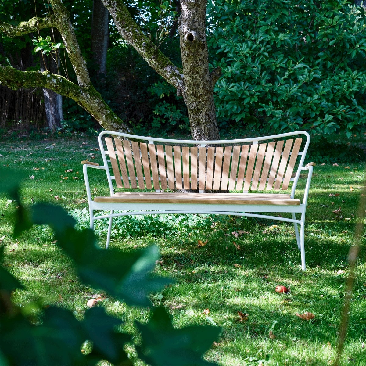 Havebænk i træ med hvidt stel, der står i en have