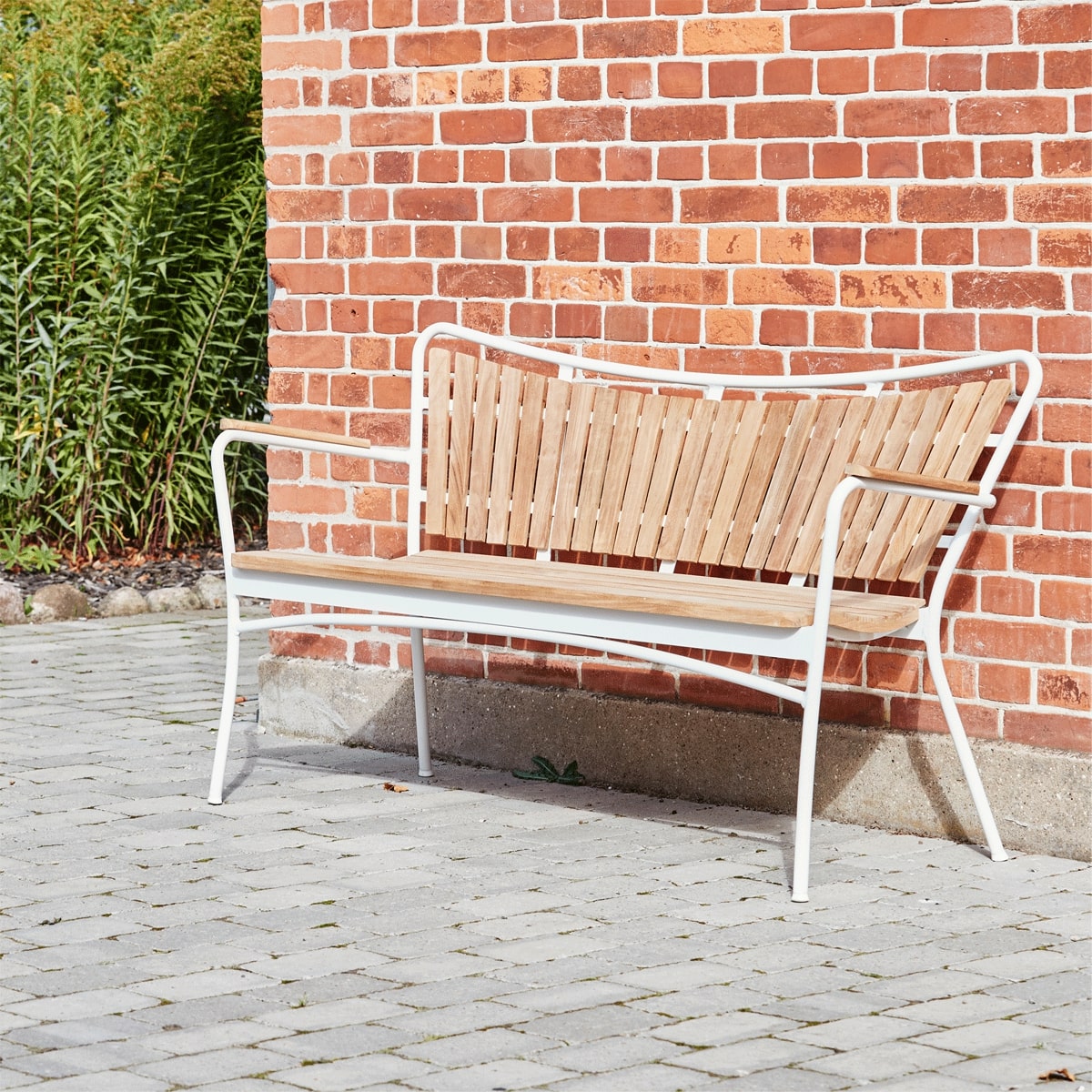 Havebænk op af husmur, bænken er i træ med hvidt stel