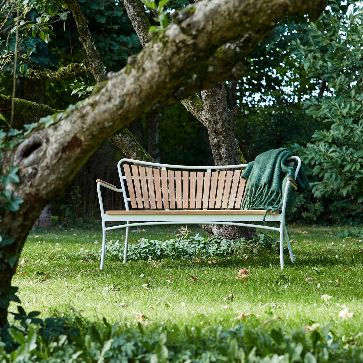 Havebænk der står i have med et grønt tæppe