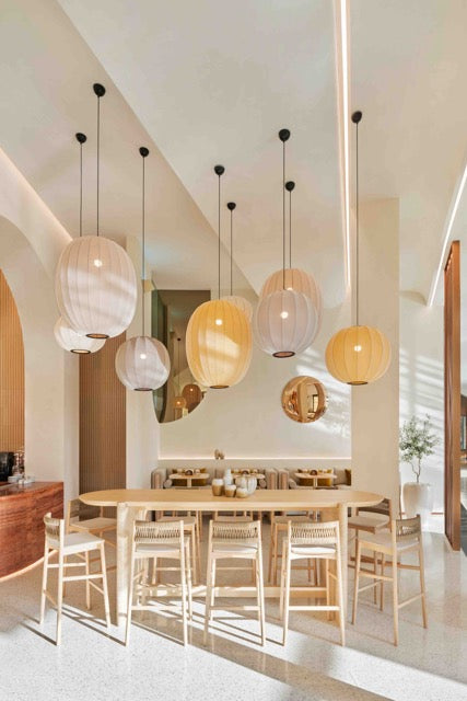 Spisestue med bord og stole i træ, med store loftlamper i pastel farver