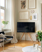 Stue med hvide vægge. TV på træstander med en billedvæg bagved, ved siden af står der en stålstol med sort stofsæde og ryglæn. I hjørnet står der et sofabord med hvid marmorbordplade. 