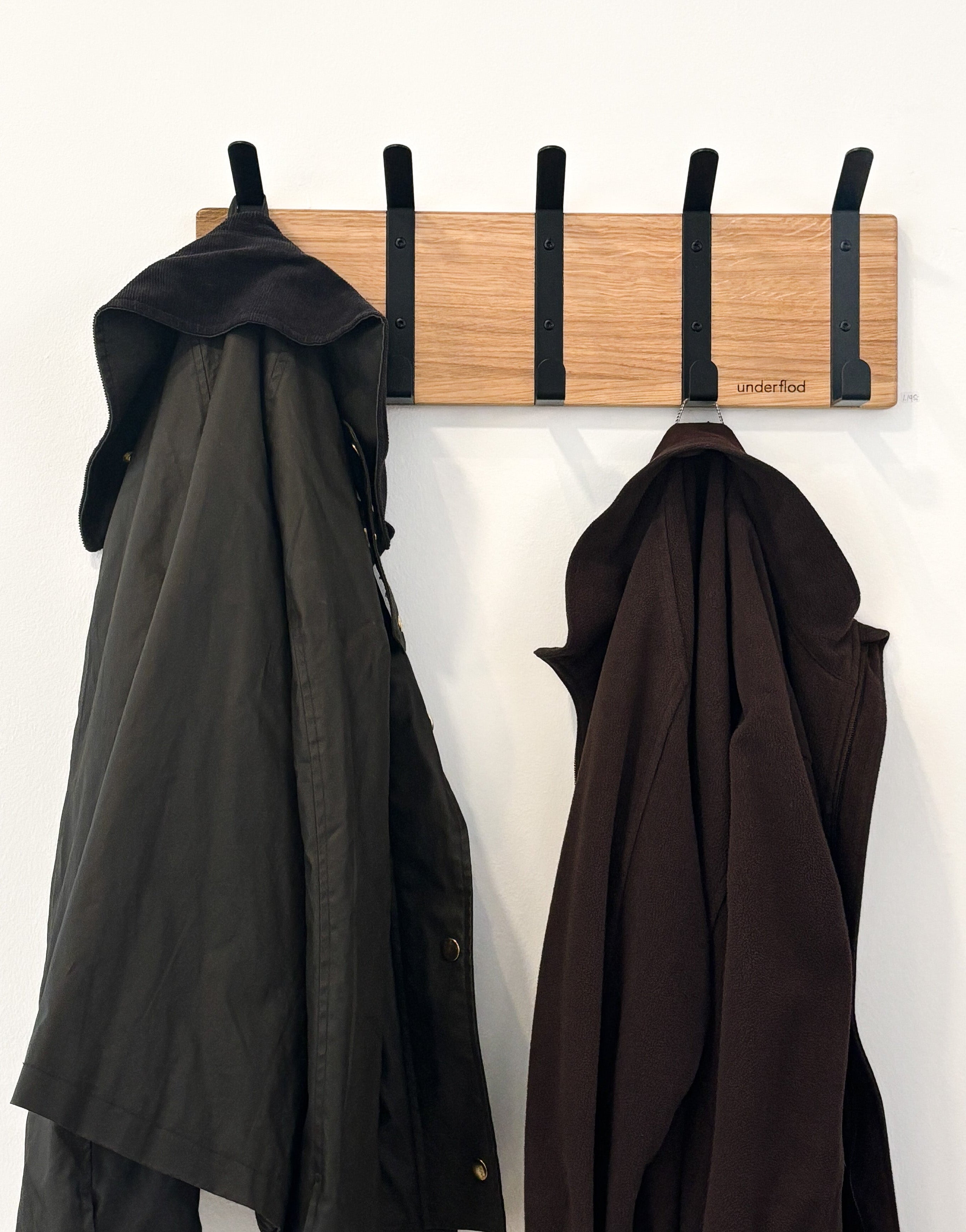 En knagerække med fem knager, hvor der hænger to jakker. 