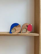 2 fugle i lys træ med blå og røde detaljer på hver fugl 