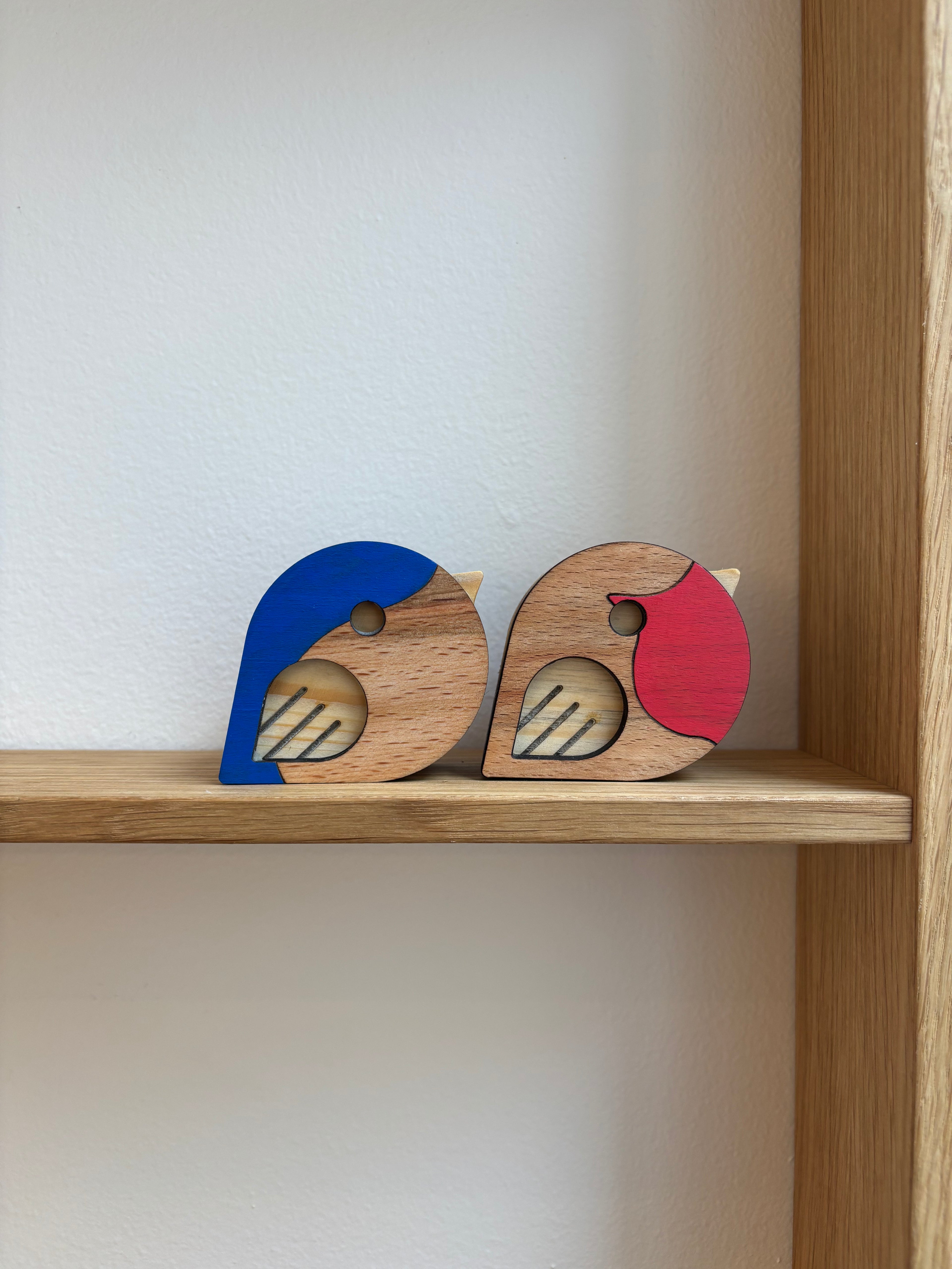 2 fugle i lys træ med blå og røde detaljer på hver fugl 