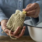 Hænder der tager en sæbebar ud af en flettet sæbepose.