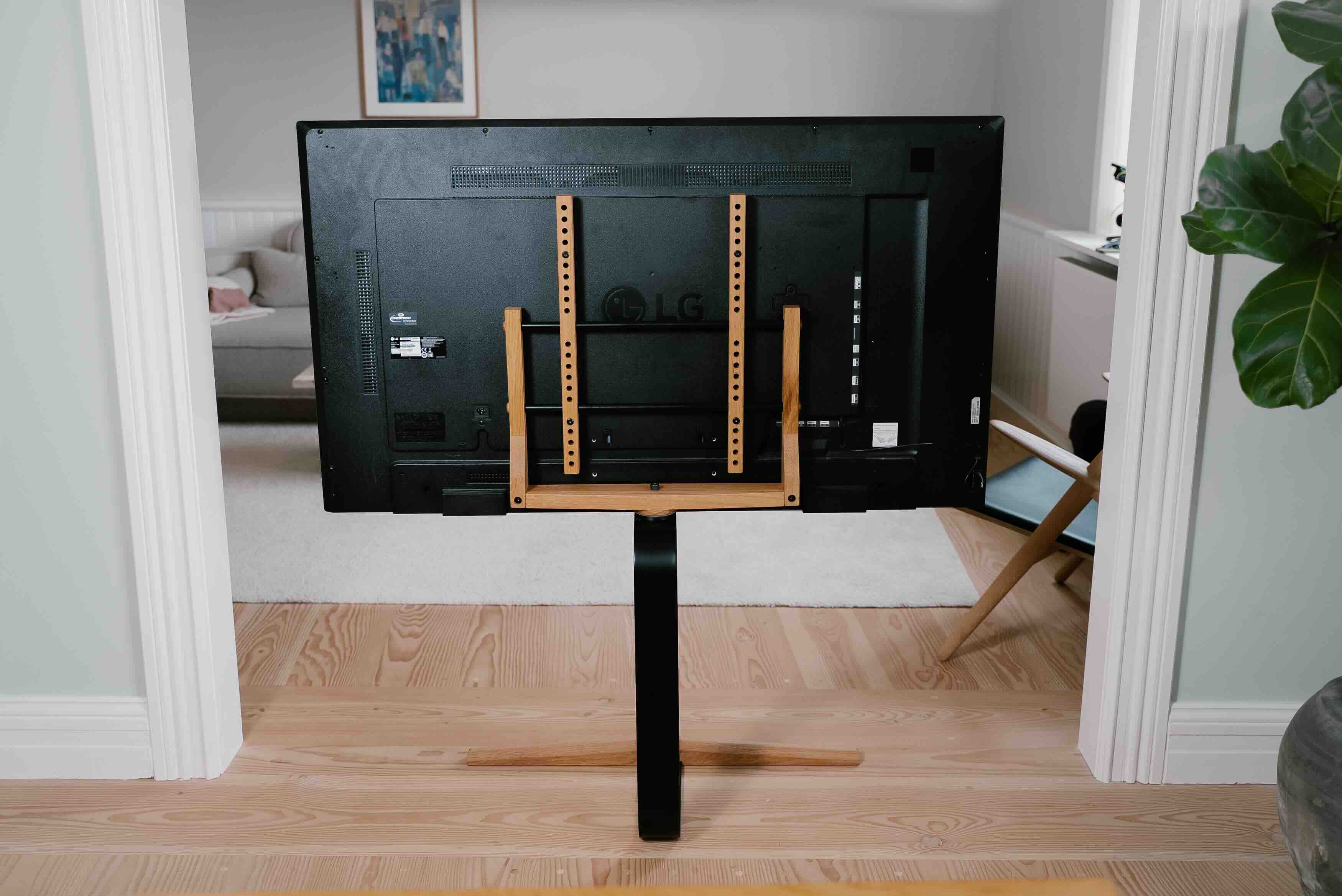 En stue hvor man ser et TV bagfra, som hænger på en tv-stander. I baggrunden kan man se sofaen og en stol. 