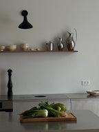 Skærebræt i træ med grøntsager på køkkenø og hylde i mørkt træ med køkkenudstyr