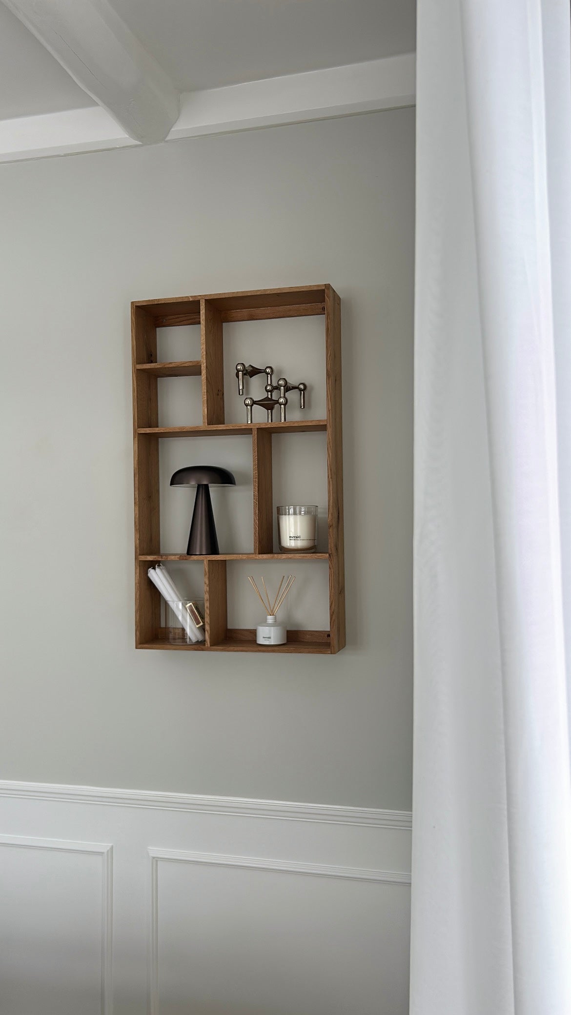 Pyntehylde i træ monteret på væggen, dekoreret med en lampe, fyrfadslys i glas og duftpinde.