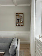 Lys og hyggelig stue med en grå sofa og en pyntehylde i træ monteret på væggen.