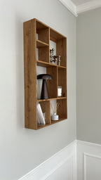 Pyntehylde i træ monteret på væggen, dekoreret med en lampe, fyrfadslys i glas og duftpinde.