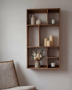 Sættekasse med 7 rum på en beige væg, i nogle af rummene er der pynt. På gulvet står der en loungestol. 