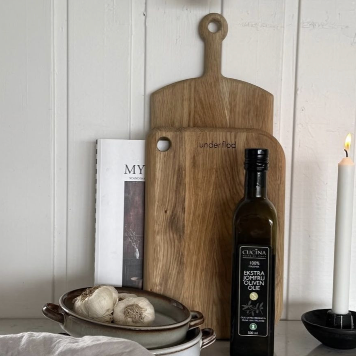 To træ tapasbrætter står op ad en hvid trævæg. Foran er nogle skåle, en olivenolie og et stearinlys. 