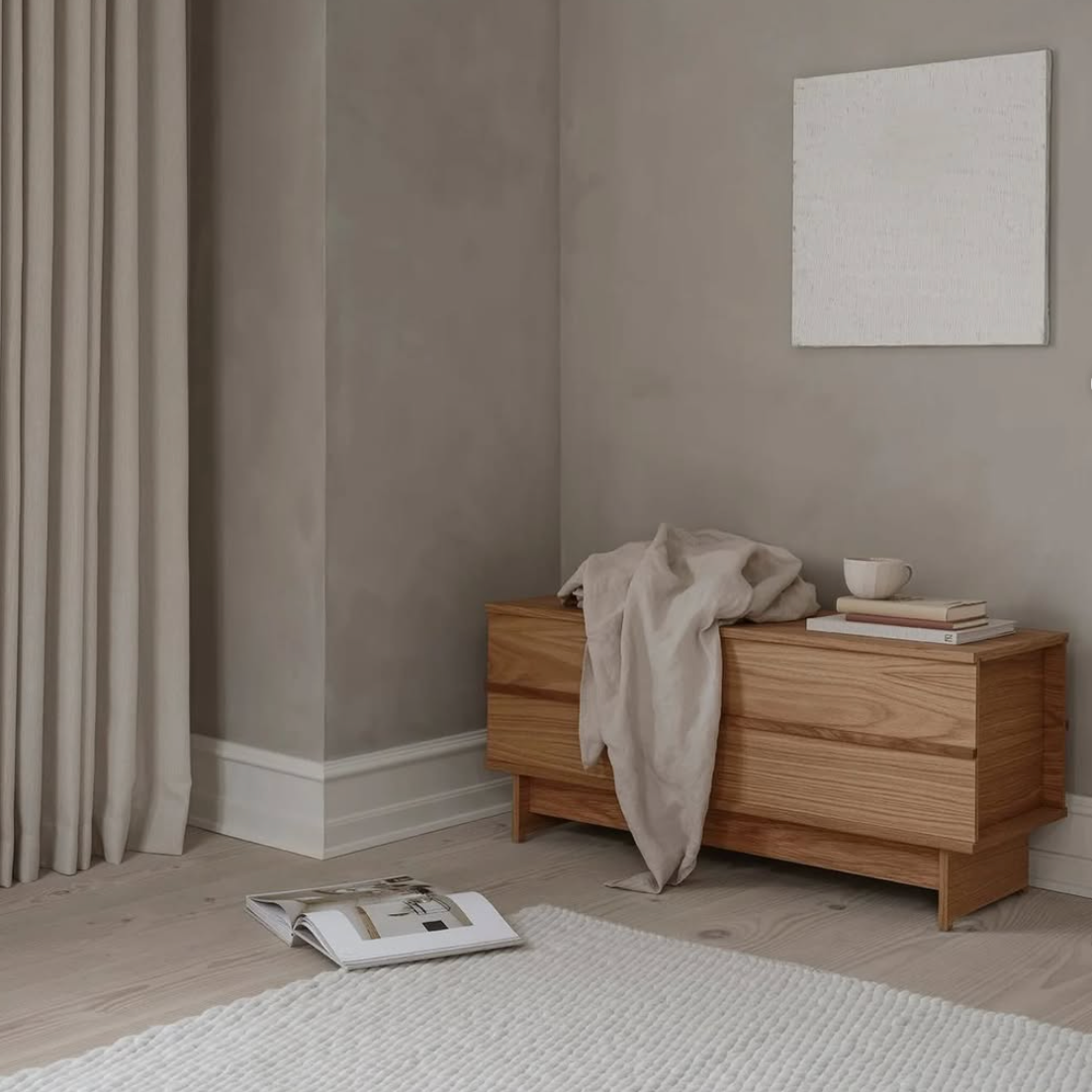 Et gråt rum med en træ kommode, hvidt gulvtæppe med et åbent magasin. På væggen hænger et hvidt lærred. 