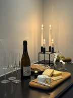 Et køkken med tre champagneglas, en flaske, et tapasbræt af træ med ost, en tallerken med knækbrød og lidt pynt. 