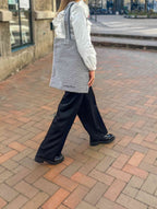 Kvinde som går udenfor på fliser med en grå mulepose, hvor der står underflod med sorte bogstaver nedst på tasken. 