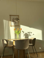 En spisestue med et bord, tre stole og en buket tulipaner. På væggen hænger en træramme på væggen med et kunsttryk af en abstrakt dame. 