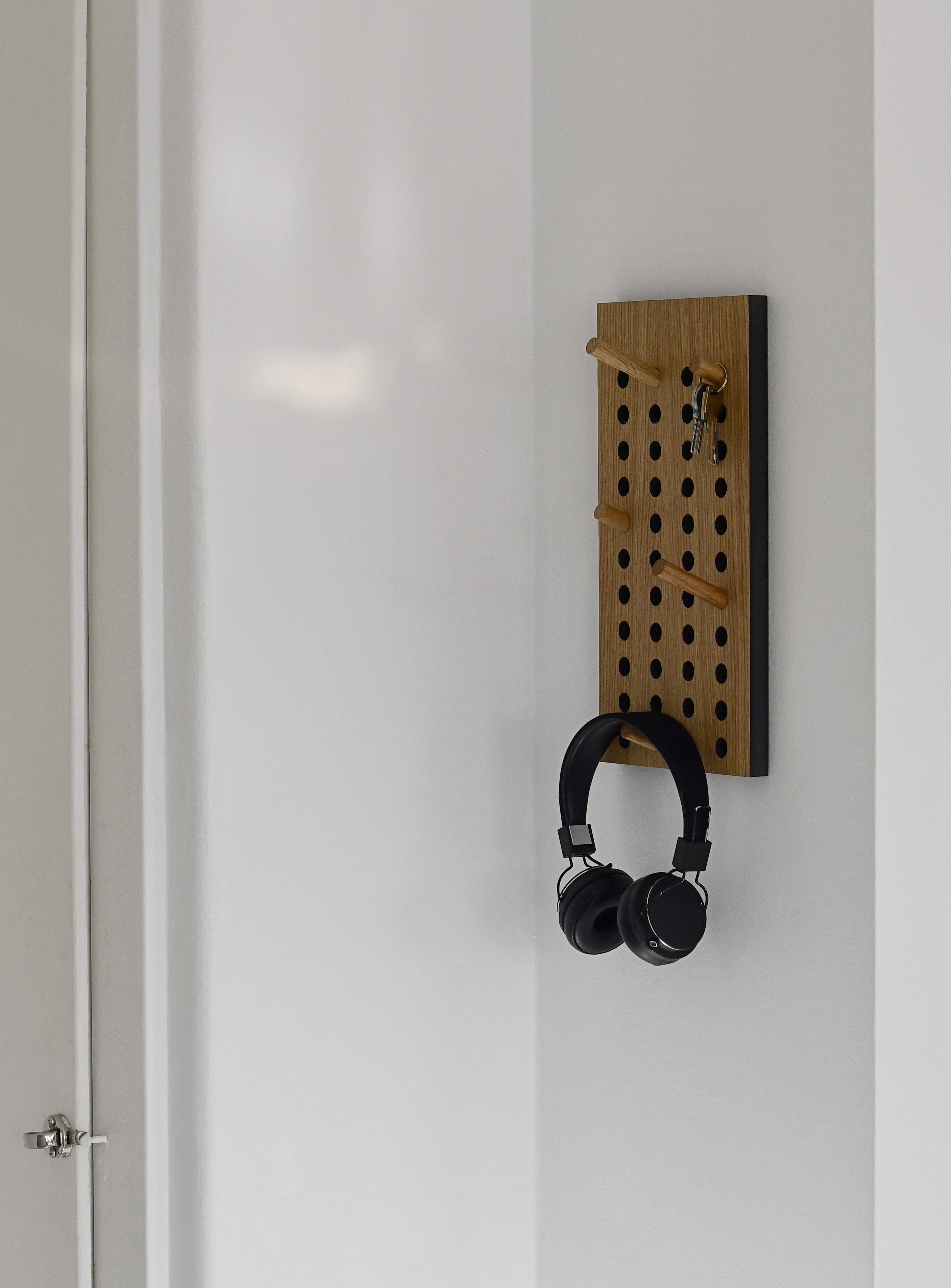 Lille scorboard knagerække på en væg, hvor der hænger nøgler og hovedtelefoner på, vist fra siden.