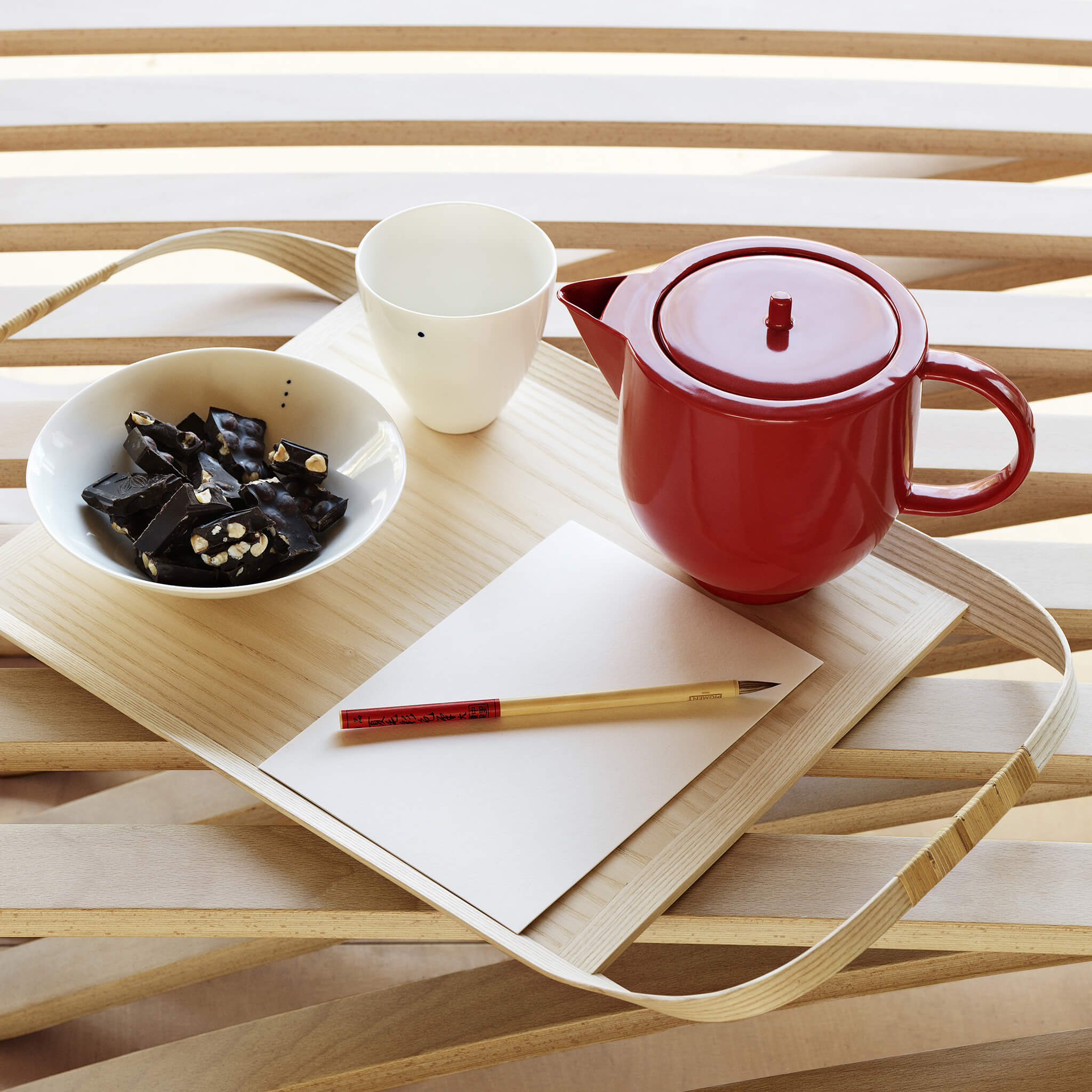 Red porcelain teapot placed on a wooden tray, next to a set of porcelain bowls